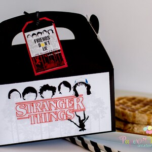 May include: Black and white Stranger Things party favor box with a red Stranger Things logo and a red tag that says "Friends Don't Lie" with a yellow sun graphic. The box is decorated with silhouettes of the characters from the show.