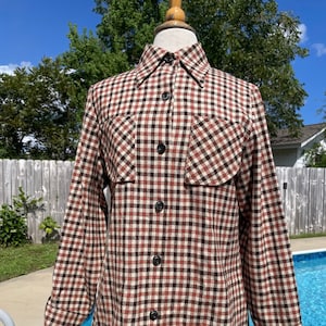 May include: A long-sleeved plaid shirt with a brown, white, and red checkered pattern. The shirt has a button-up front and two flap pockets on the chest.