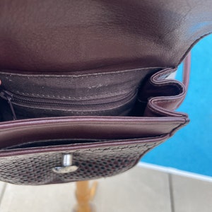 May include: A brown leather purse with a woven pattern and a silver clasp. The purse has a zippered pocket on the inside.