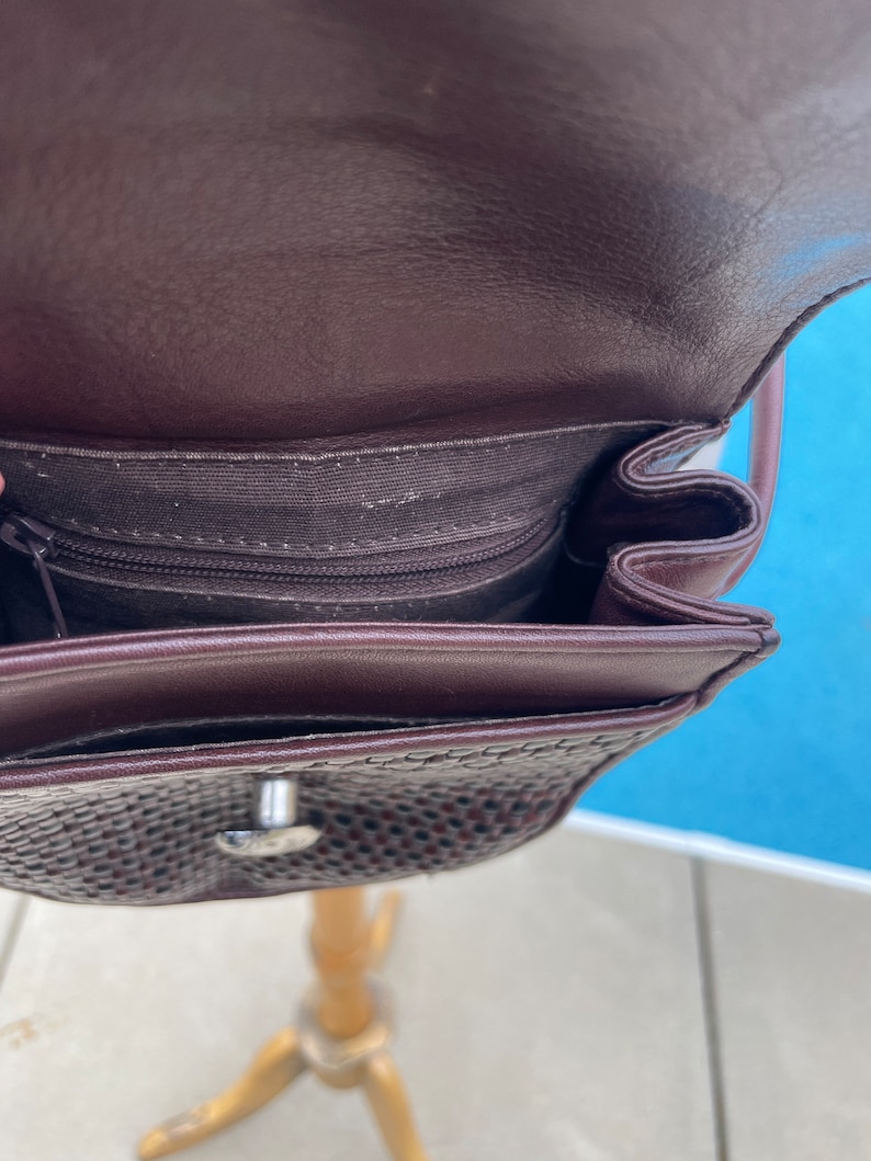 May include: A brown leather purse with a woven pattern and a silver clasp. The purse has a zippered pocket on the inside.