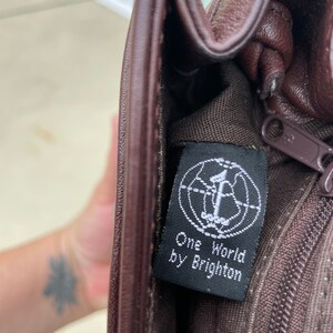 May include: A brown leather purse with a black tag that reads "One World by Brighton".
