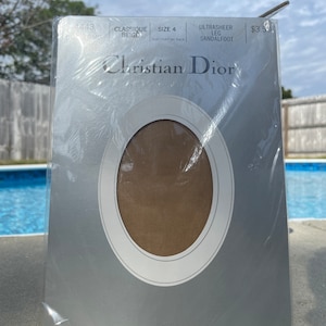 May include: A package of Christian Dior Ultrasheer Leg Sandalfoot tights in the color Classique Beige, size 4. The package is silver with a white oval cutout showing the color of the tights.