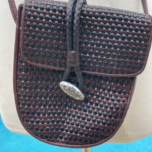 May include: A brown and black woven leather crossbody bag with a silver clasp. The bag has a braided leather strap.
