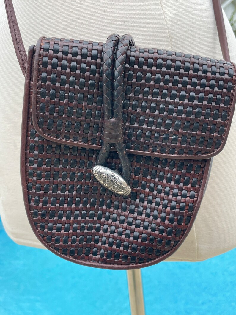 May include: A brown and black woven leather crossbody bag with a silver clasp. The bag has a braided leather strap.