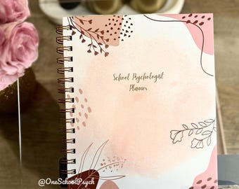May include: A spiral-bound planner with a soft pink and white watercolor design. The cover features floral and abstract shapes in shades of brown and pink, with the text "School Psychologist Planner". The planner is displayed on a clear stand.