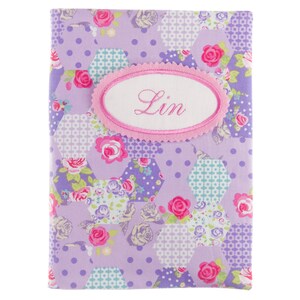 Könnte beinhalten: Ein lilafarbenes Stoffjournal mit einem rosa ovalen Patch, auf dem "Lin" steht, und einem Blumenmuster.