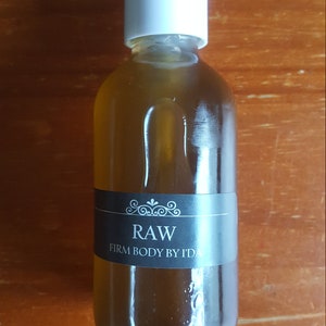 Może przedstawiać: Przezroczysta szklana butelka z białą pompką. Butelka zawiera jasnobrązowy płyn. Etykieta na butelce głosi "RAW FIRM BODY BY IDA".