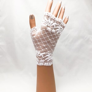 Puede incluir: Guantes sin dedos de encaje blanco con un delicado dise&ntilde;o floral y un dise&ntilde;o de red en forma de diamante. Los guantes se muestran en una mano de maniqu&iacute; sobre un fondo blanco. Un accesorio nupcial.