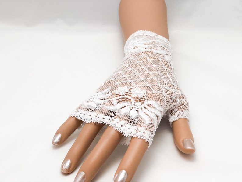 Puede incluir: Guantes sin dedos de encaje blanco con dise&ntilde;o floral. Los guantes est&aacute;n hechos de encaje delicado de tejido abierto. Cubren la mano hasta los nudillos, dejando los dedos expuestos.