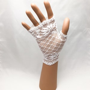 Puede incluir: Guantes sin dedos de encaje blanco con un delicado dise&ntilde;o floral en los bordes y un dise&ntilde;o de red en forma de diamante. Los guantes se muestran en una mano de maniqu&iacute; sobre un fondo blanco.