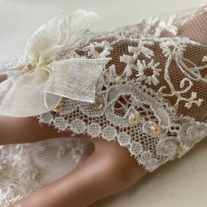 Puede incluir: Guantes sin dedos de encaje marfil con bordados florales y lentejuelas iridiscentes. Un lazo transparente adorna la parte superior del guante. Los guantes son un accesorio delicado, perfecto para bodas u ocasiones especiales.