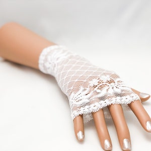 Puede incluir: Guantes sin dedos de encaje blanco con un dise&ntilde;o floral en el pu&ntilde;o y un patr&oacute;n de malla de diamantes. Los guantes se muestran en una mano de maniqu&iacute; con u&ntilde;as pintadas, sobre un fondo blanco.