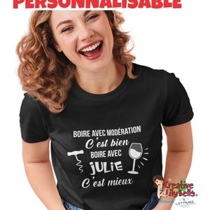 Peut inclure: T-shirt noir avec un texte blanc qui dit "Boire avec modération C'est bien Boire avec Julie C'est mieux". Le texte est accompagné d'un graphique d'un verre à vin et d'un tire-bouchon.