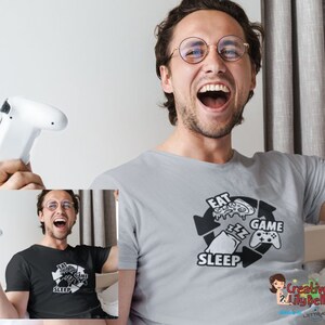 May include: A gray t-shirt with a graphic of a circle with arrows pointing to the words "Eat", "Game", "Sleep", and a pizza slice, a controller, and a pillow inside the circle.