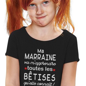 Peut inclure: T-shirt noir avec du texte blanc qui dit "Ma Marraine va m'apprendre toutes les BÊTISES qu'elle connaît! J'EN AI POUR LONGTEMPS!!" avec une étoile rouge de chaque côté du mot "BÊTISES". Le texte "Creative Lily Bells" est dans le coin inférieur droit du t-shirt.