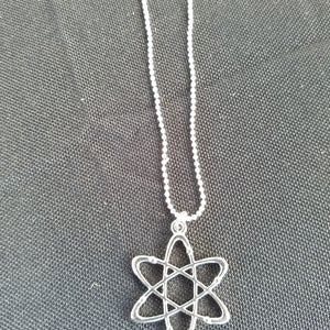 May include: A silver chain necklace with an atom pendant. The atom is a simple design with a circle in the center and lines extending out to form a star shape.