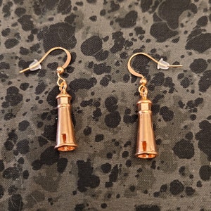 May include: A pair of gold-toned earrings shaped like lighthouses. The earrings have a simple design and are a great addition to any jewelry collection.