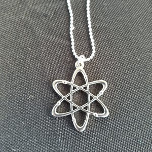 May include: A silver necklace with an atom pendant. The atom is a simple design with a circle in the center and five rings around it.