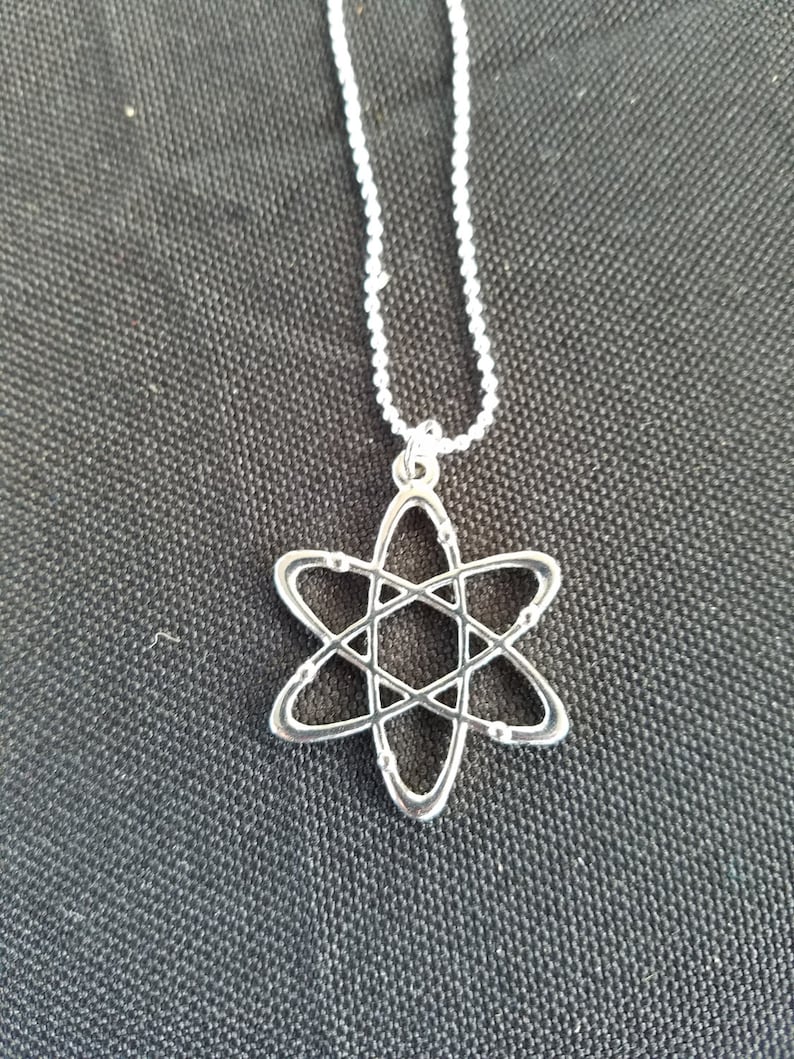 May include: A silver necklace with an atom pendant. The atom is a simple design with a circle in the center and five rings around it.