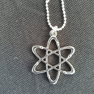 May include: A silver necklace with a silver atom pendant. The atom is a simple design with a circle in the center and lines extending out to form a star shape.