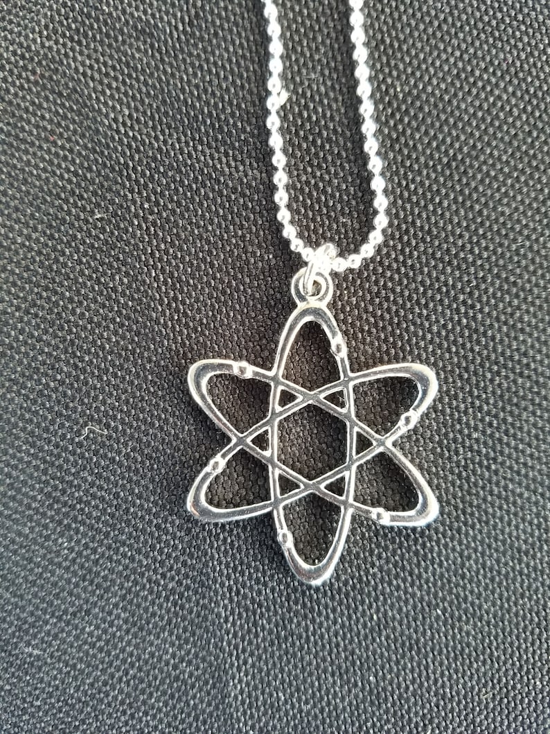 May include: A silver necklace with a silver atom pendant. The atom is a simple design with a circle in the center and lines extending out to form a star shape.