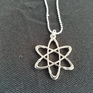 May include: A silver necklace with an atom pendant. The atom is a simple design with a circle in the center and lines extending out to form a star shape.