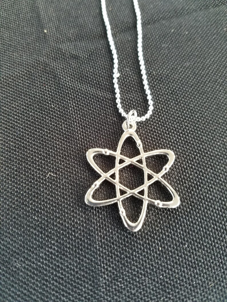 May include: A silver necklace with an atom pendant. The atom is a simple design with a circle in the center and lines extending out to form a star shape.