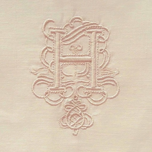 Puede incluir: Primer plano de un textil rosa pálido con una letra "H" bordada en un estilo vintage ornamentado. El bordado es en hilo rosa pálido a juego. El borde inferior presenta una fila de pequeños agujeros espaciados.