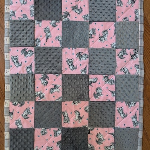 May include: A pink and grey baby quilt with a patchwork design featuring kittens. The quilt is made of soft, plush fabric and is perfect for cuddling.