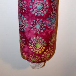 May include: A pink reusable grocery bag with a white drawstring and a colorful floral pattern. The pattern features blue, green, and yellow flowers on a pink background.