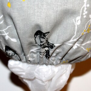 May include: A gray fabric trash bag dispenser with a white and black floral pattern featuring birds. The dispenser has a white plastic bag attached.