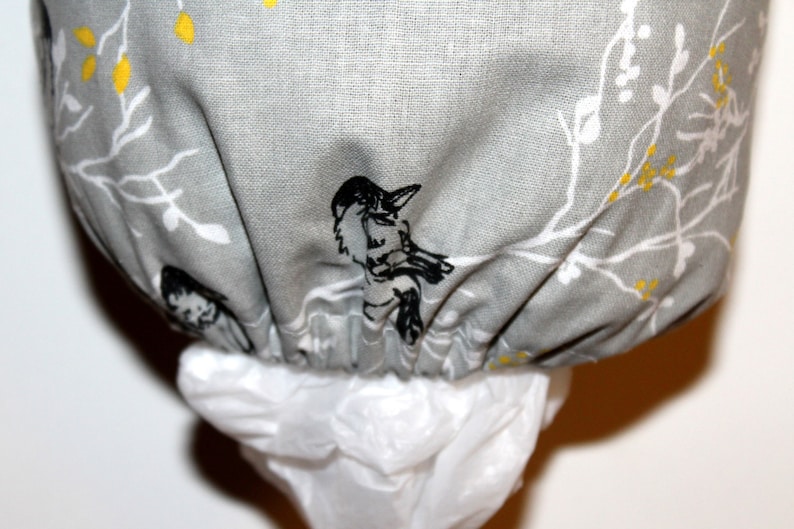 May include: A gray fabric trash bag dispenser with a white and black floral pattern featuring birds. The dispenser has a white plastic bag attached.