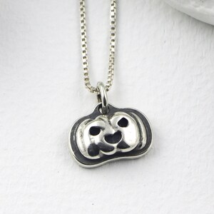 May include: A silver pendant necklace with a pumpkin charm. The charm is a detailed carving of a pumpkin face. The necklace has a fine box chain. The pumpkin charm is a Halloween-themed item.