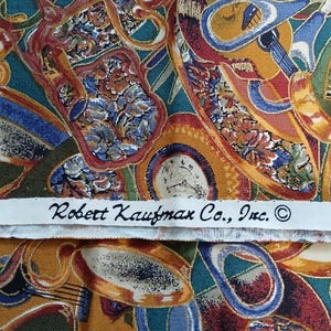 May include: A colorful fabric with a repeating pattern of clocks, musical instruments, and other decorative elements. The fabric has a teal, blue, orange, and red color scheme. The fabric has a label that reads "Robert Kaufman Co., Inc. ©".