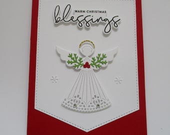 Könnte beinhalten: Eine Weihnachtskarte mit rotem Rand und weißer Mitte. Die weiße Mitte zeigt einen ausgestanzten Engel mit goldenem Heiligenschein, grünen und roten Akzenten und den Worten "blessings" und "Warm Christmas".