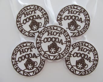 May include: Five brown and white circular ornaments with the words "Cozy Warm Hot Cocoa" and a cocoa cup design. Each ornament has a white scalloped edge and a white ribbon for hanging.