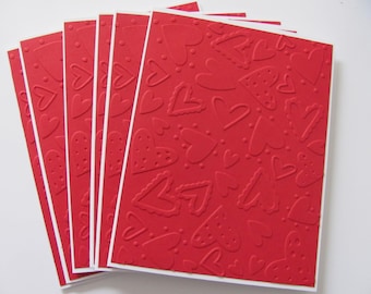 May include: A stack of red greeting cards with embossed heart patterns. The cards have a white border and are fanned out, showcasing various heart designs, including dotted and scalloped edges. Ideal for Valentine's Day or other romantic occasions.