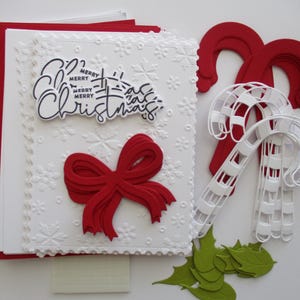 K&ouml;nnte beinhalten: Ein festliches Weihnachtskartenset mit wei&szlig;em Pr&auml;gedesign, roter Schleife und dem Schriftzug "Merry Christmas". Enth&auml;lt rote Umschl&auml;ge, Zuckerstangen-Dekorationen, gr&uuml;ne Stechpalmenbl&auml;tter und rote Pailletten.