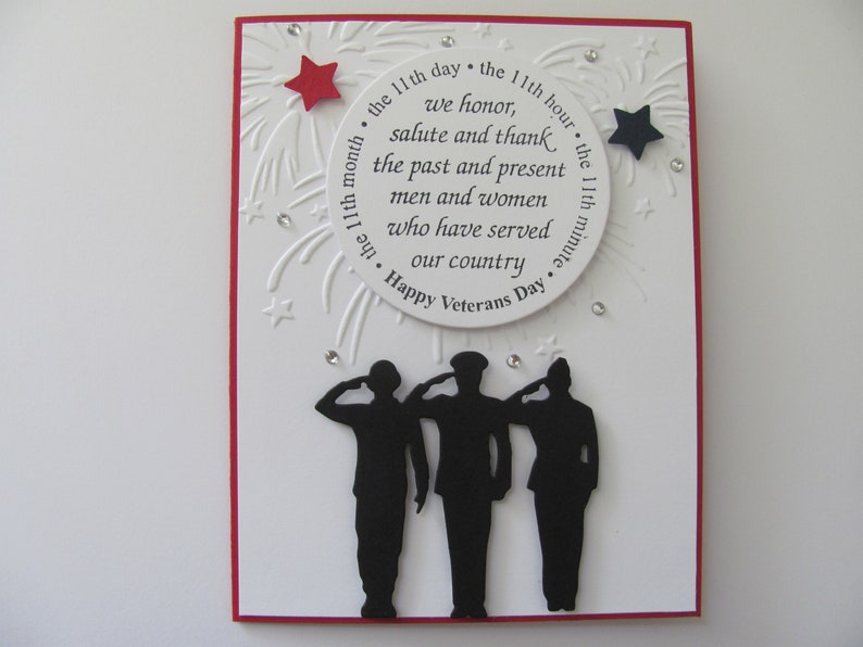 May include: Veterans Day card featuring three silhouetted soldiers saluting.  The card is predominantly white with red accents. A circular design element includes the text: 'the 11th day • the 11th hour • the 11th month • the 11th minute. We honor, salute and thank the past and present men and women who have served our country. Happy Veterans Day'.  Red and black stars embellish the design.