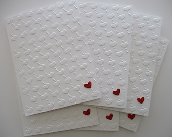 May include: Set of six white cards with a repeating pattern of embossed hearts. Each card has a single red glitter heart in the center.