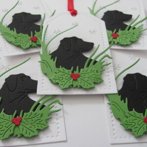 May include: Five white gift tags with a black silhouette of a dog, green holly leaves, and red berries. The tags are decorated with a white dotted border.
