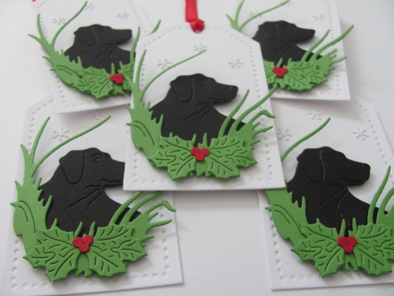 May include: Five white gift tags with a black silhouette of a dog, green holly leaves, and red berries. The tags are decorated with a white dotted border.
