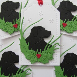 May include: Five white gift tags with black silhouettes of Labrador Retrievers, green holly leaves, and red berries. The tags are decorated with a white snowflake pattern.
