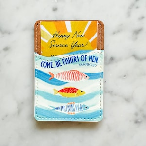 Puede incluir: Un tarjetero con la parte superior de corcho y un frente con estampado azul y blanco. El frente presenta tres peces coloridos nadando en líneas onduladas azules, con el texto "COME...BE FISHERS OF MEN" y "Happy New Service Year!"