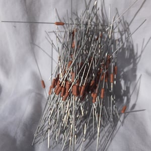 May include: A pile of electronic components, specifically axial lead resistors, with silver leads and brown cylindrical bodies. The resistors are scattered on a white surface, casting shadows.