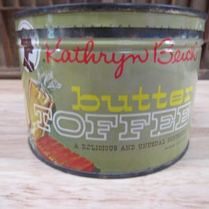 May include: A vintage green metal tin with a yellow and white label that reads "Kathryn Beich's Butter Toffee A Delicious and Unusual Confection Made in U.S.A."
