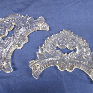May include: Two clear glass crystal prisms with a cut-out design. The prisms are shaped like a crescent moon and have a floral pattern.