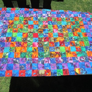 May include: A rectangular quilt constructed from a grid of multicolored fabric squares featuring various floral and abstract patterns. Small, circular blue buttons are sewn at the intersections of many of the fabric squares across the surface.
