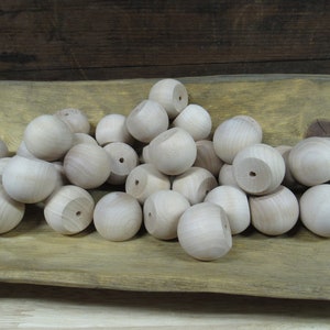 May include: A pile of 20 natural wood round balls with a small hole drilled through the center of each ball. The balls are arranged in a bowl on a wooden surface.