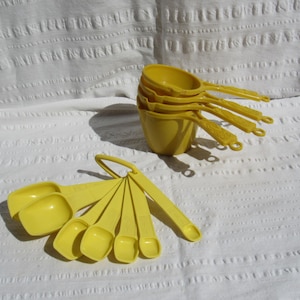 May include: A collection of bright yellow measuring cups and spoons. The cups are stacked, and the spoons are fanned out. The kitchen tools are made of plastic and are designed for baking and cooking. The set includes various sizes for precise measurements.